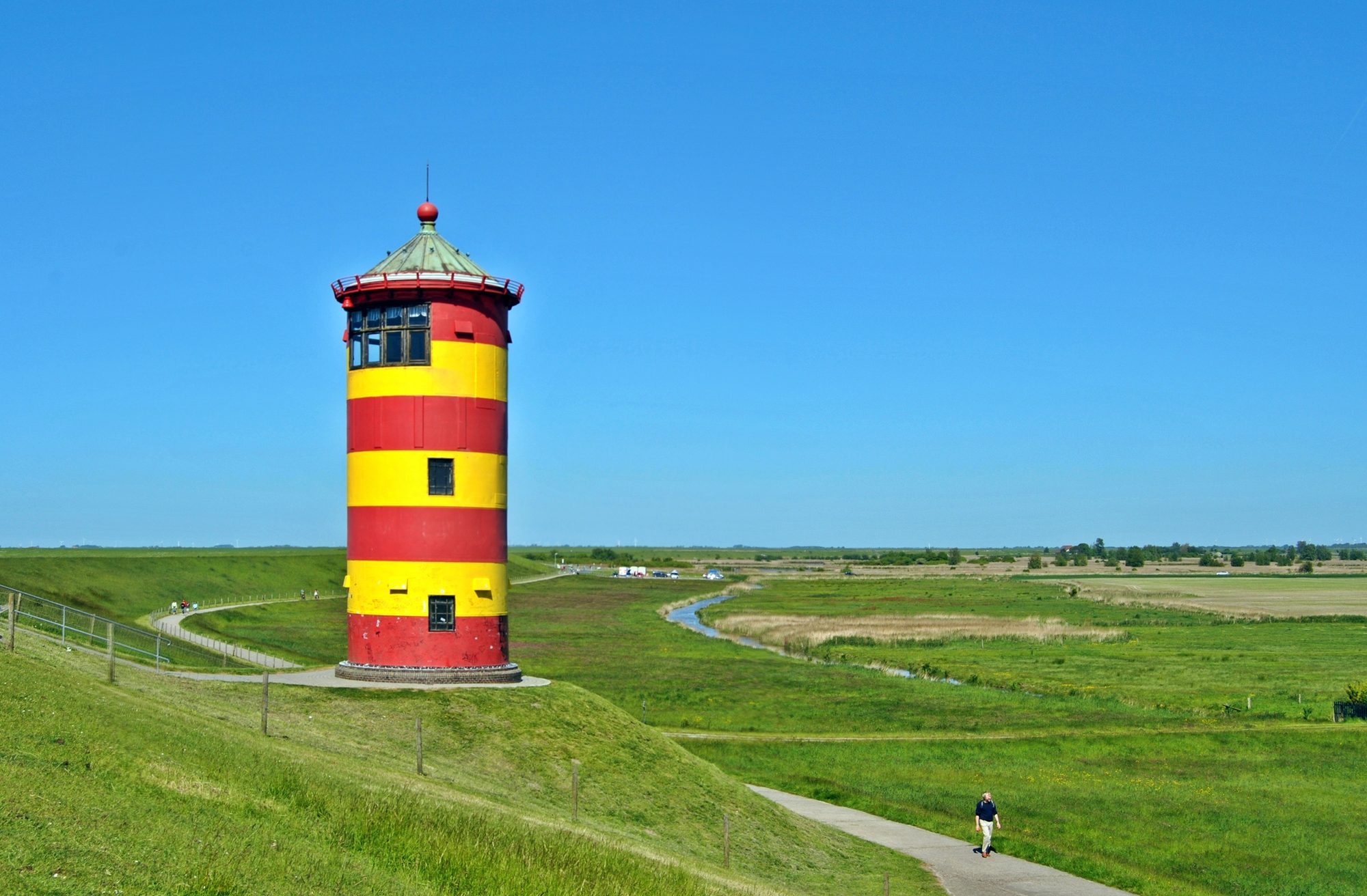Der rot-gelbe Pilsumer Leuchtturm auf dem grünen Nordseedeich in der Krummhörn